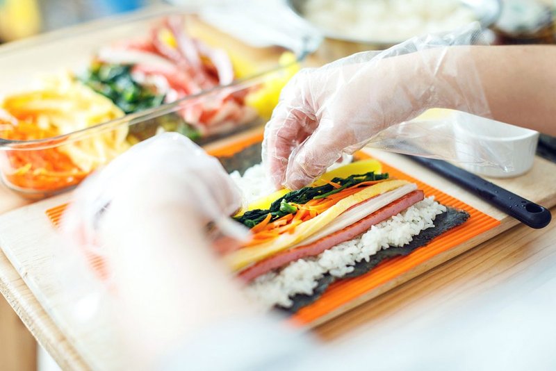 Bạn xếp các nguyên liệu lên trên lá rong biển và cuộn cơm với lực tay vừa phải. Xếp các nguyên liệu lên trên lá rong biển và cuộn với lực tay vừa phải là cách làm cơm cuộn chiên giòn chuẩn