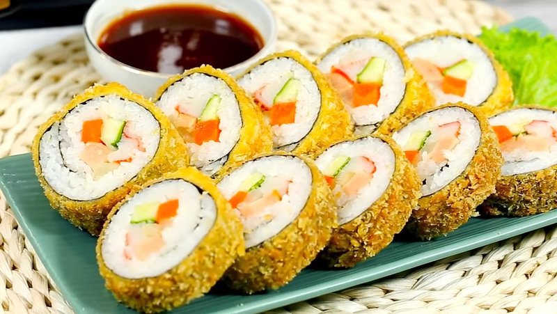 Lớp vỏ cơm cuộn chiên xù giòn rụm ôm trọn phần nhân thơm béo của thanh cua, xúc xích và rau củ, mang đến cảm giác giòn, mềm, đậm đà khó cưỡng. Lớp vỏ cơm cuộn chiên xù giòn rụm ôm trọn phần nhân thơm béo của thanh cua, xúc xích và rau củ, mang đến cảm giác giòn, mềm, đậm đà khó cưỡng.